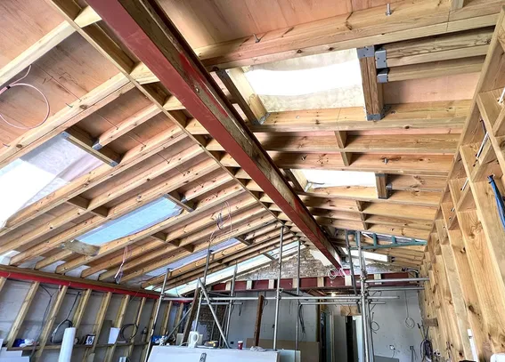 A photograph of a home extension during construction. It shows a timber frame structures with a lot of rooflights inside a pitched roof and three steel beams to support the space.
