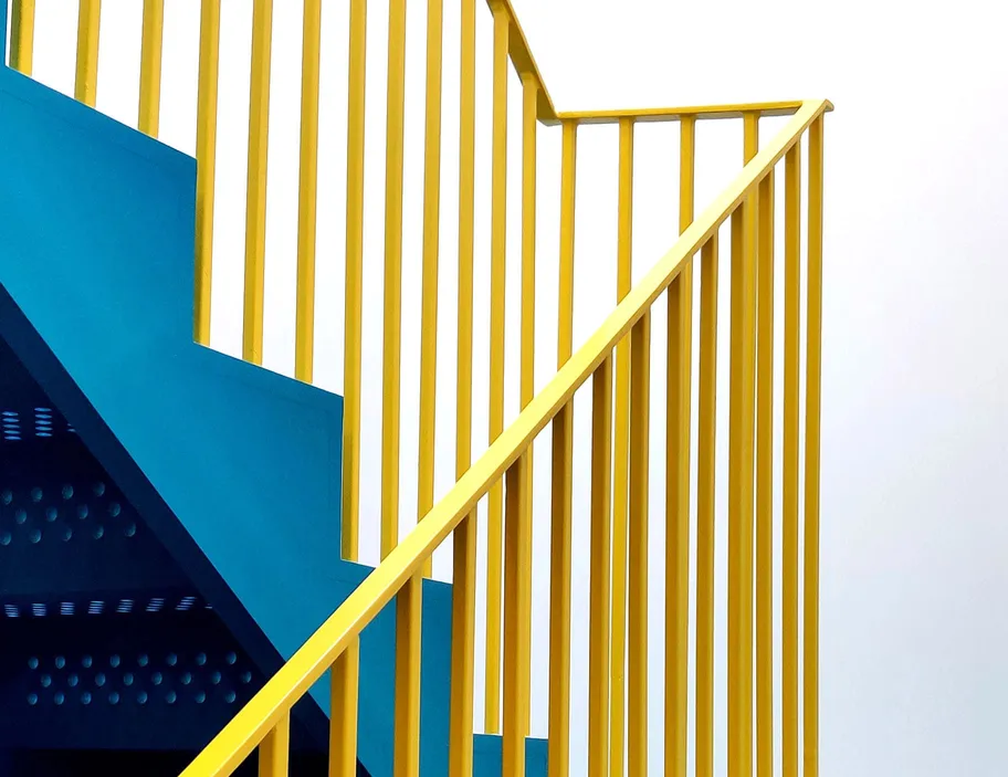 A vibrant yellow stair railing against a minimalist blue and white background.